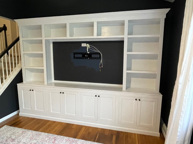 A white wooden TV shelf positioned near the staircase against a black wall, creating a striking contrast in the room's decor