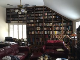 A bookshelf filled with numerous books, complemented by a maroon sofa set, creating a cozy reading nook in the room